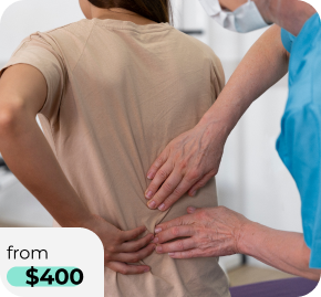 Person in a beige shirt has their back to the camera as a medical professional in blue scrubs applies pressure to their lower back.