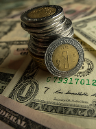Close-up of a stack of bi-metallic Euro coins with a single 1-Euro coin leaning against them, set on top of scattered U.S. dollar banknotes.