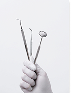 A gloved hand holding several stainless steel dental instruments, including a dental mirror and probes, against a pale background.